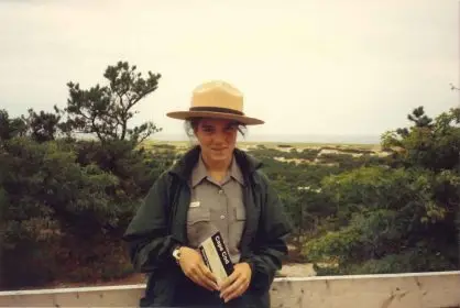 A park ranger standing in front of some dunes and forest.